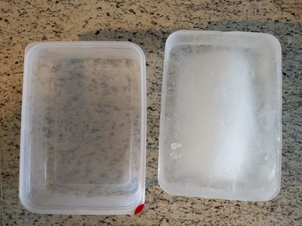 A block of ice rests on a counter next to a plastic tupperware mold