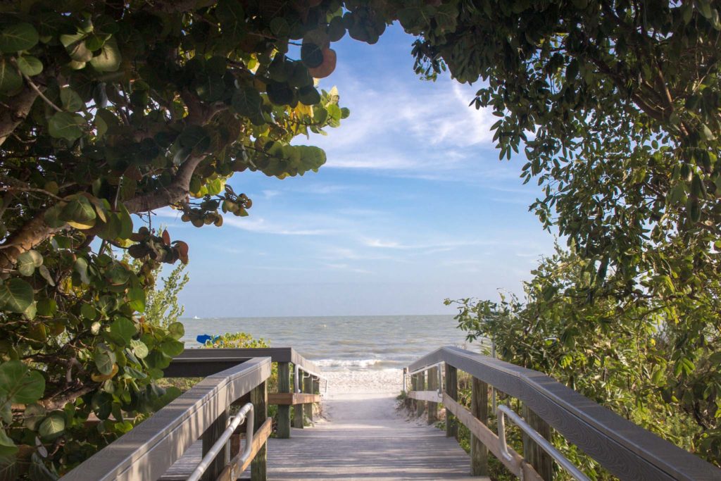 Sanibel Island Beaches are visible through green trees and a beach walkway