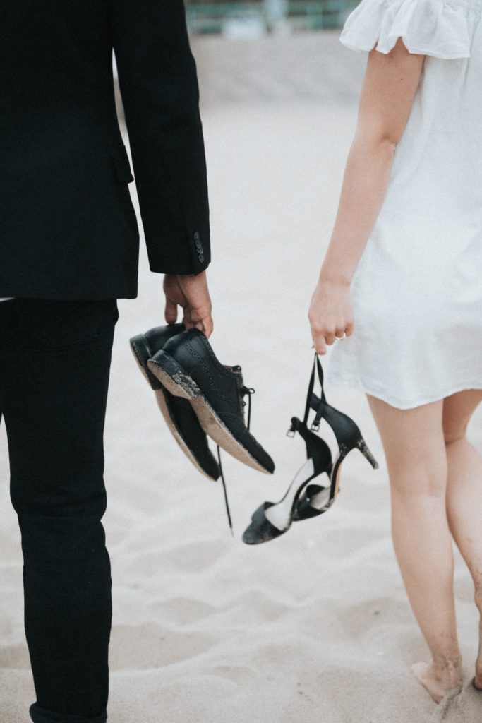 A barefoot bride and groom hold their shoes as they get married on a beach.